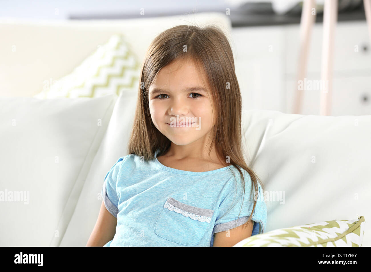 Portrait of cute little girl sitting on sofa at home Stock Photo - Alamy