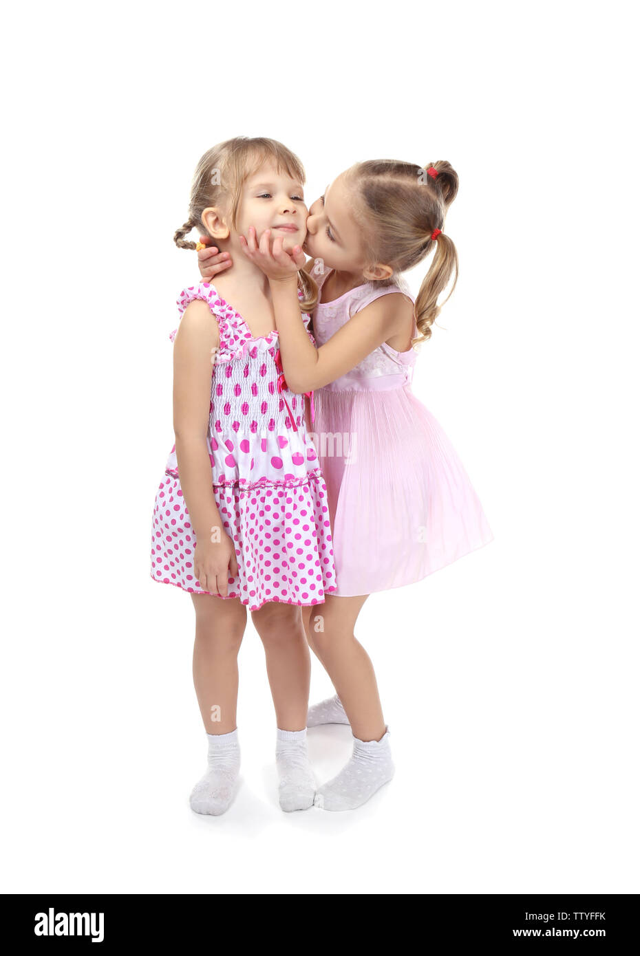 Adorable little sisters in beautiful dresses kissing on white background Stock Photo