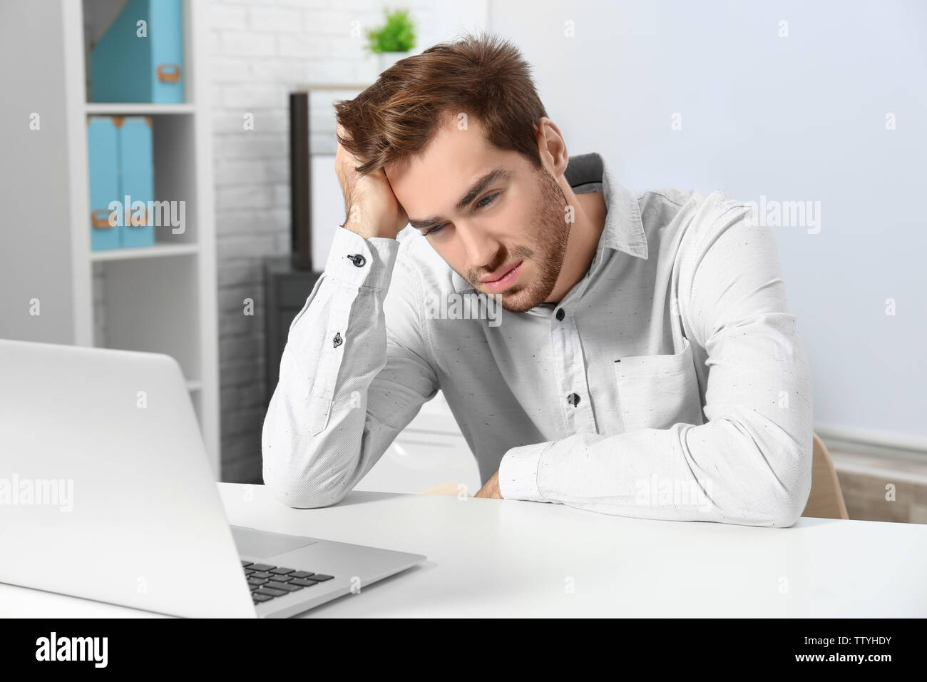 Tired handsome man working with laptop in office Stock Photo