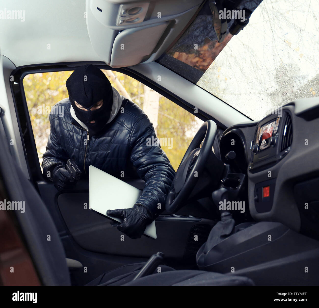 Thief in mask stealing laptop from a car Stock Photo - Alamy