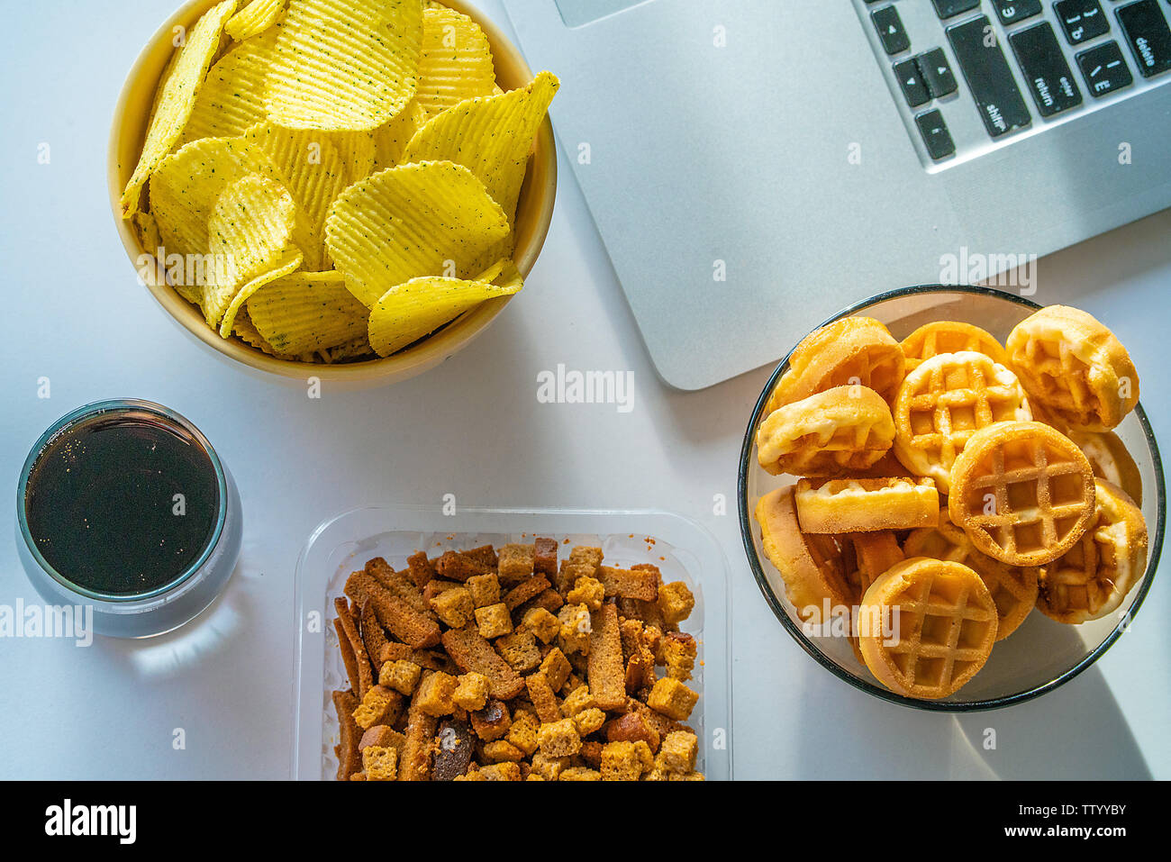 Bad habit. Work space with laptop, candies, chips, cola on white background. Junk food Stock