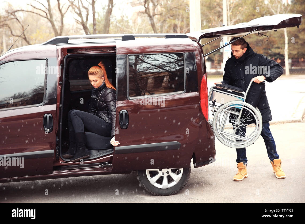 Young man loading wheelchair of handicapped woman into car Stock Photo