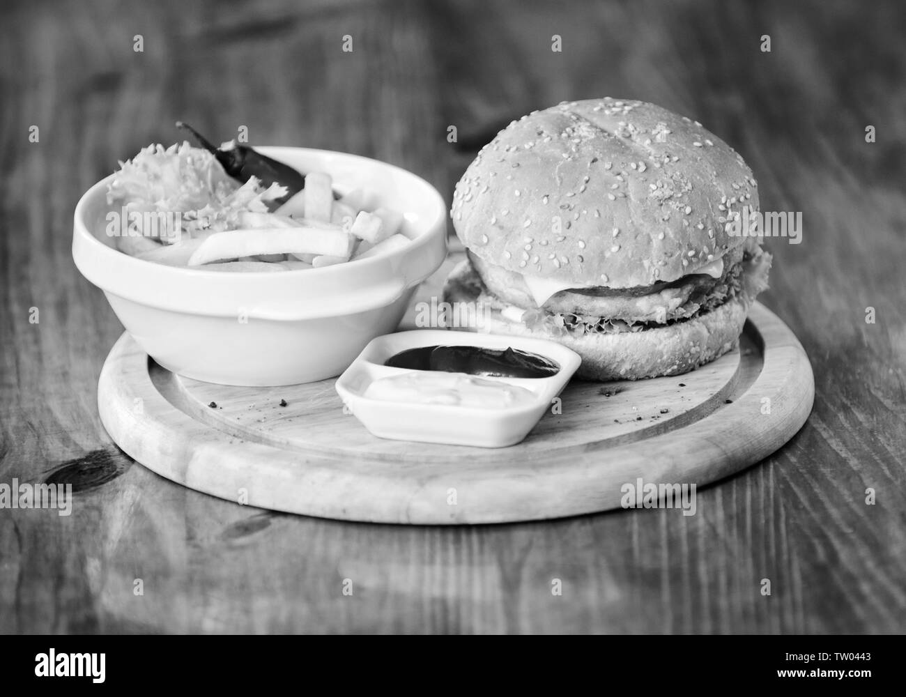 Fast food concept. High calorie snack. Burger menu. Hamburger with sesame seeds and french fries and tomato sauce on wooden board. Delicious burger. Burger with cheese meat and salad. Pub food. Stock Photo