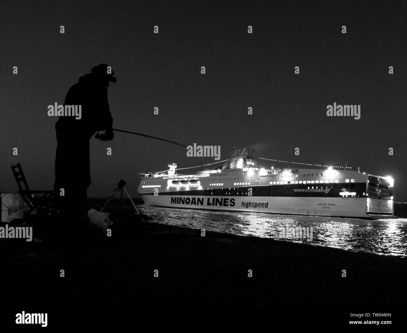 Silhouette of a man fishing from the pier with a Minoan lines ship exiting the harbour in the background. Heraklion, Crete, Greece. Stock Photo