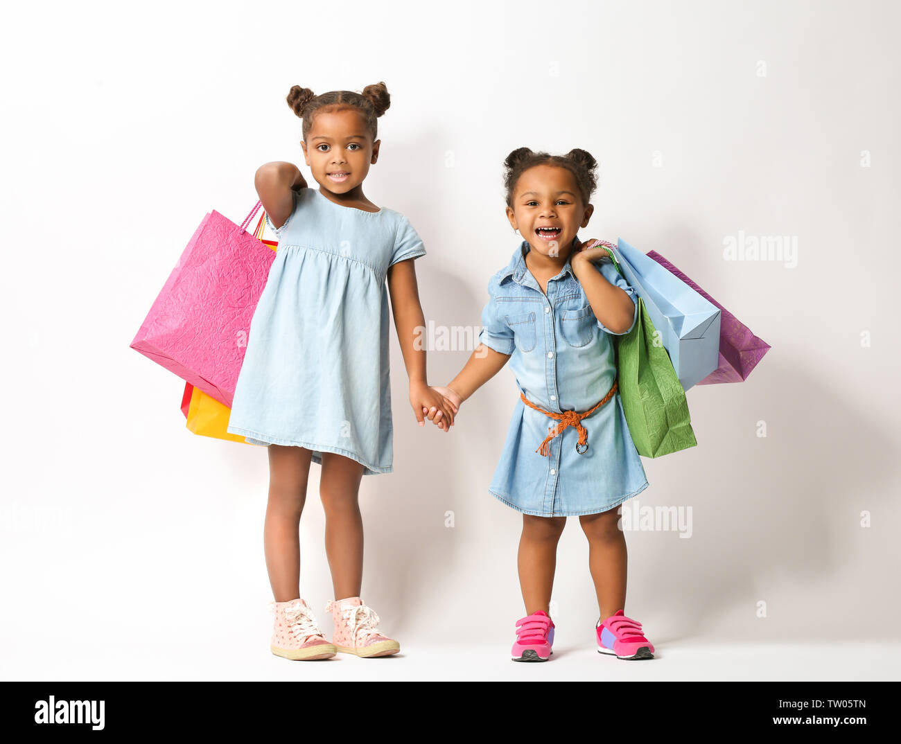Two cute African girls with shopping bags on white background Stock Photo