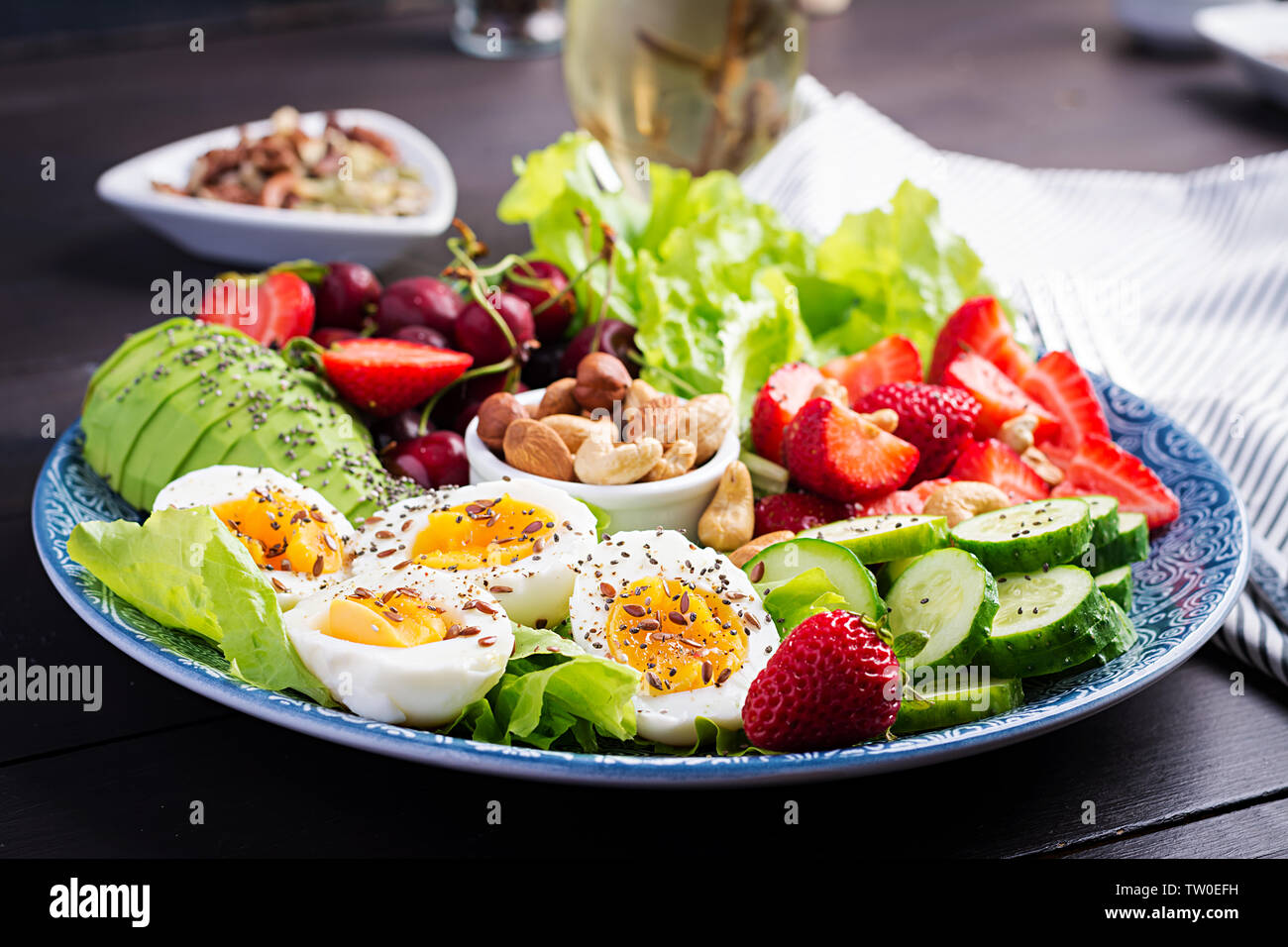 Plate with a paleo diet food. Boiled eggs, avocado, cucumber, nuts, cherry and strawberries. Paleo breakfast. Stock Photo