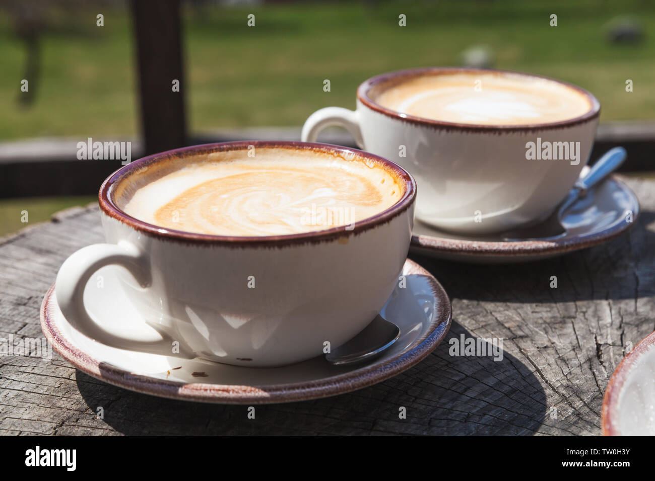 Two cups of cappuccino coffee stand on wooden table, outdoor breakfast Stock Photo