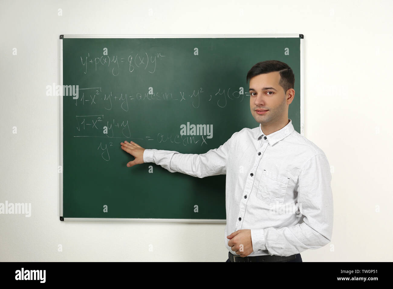 Handsome young teacher explaining math formulas written on blackboard Stock Photo
