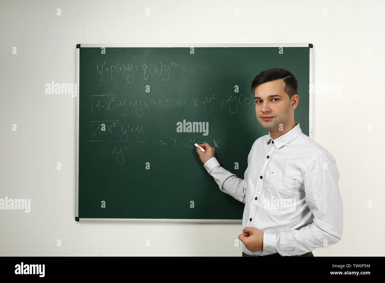 Handsome young teacher explaining math formulas written on blackboard Stock Photo