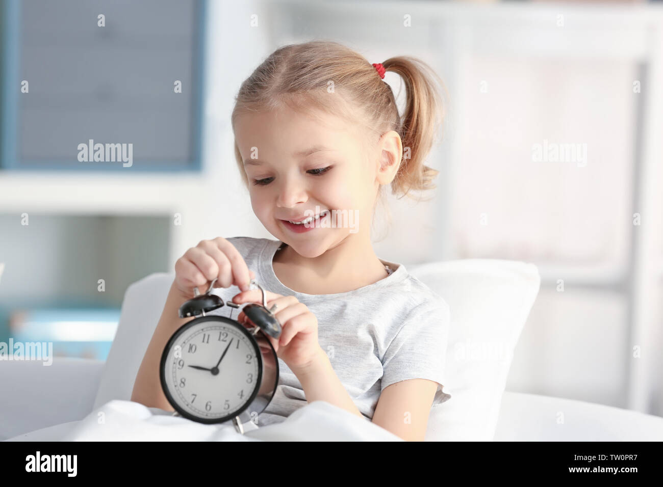 Cute little girl with alarm clock in bed Stock Photo Alamy