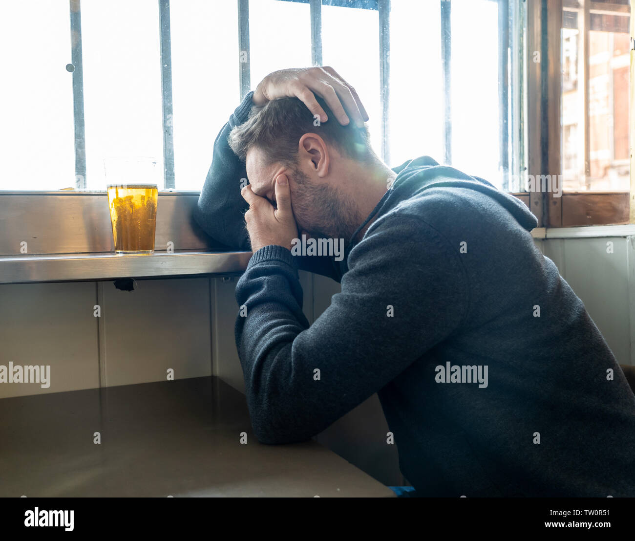 Portrait of a attractive caucasian man drinking beer in a bar pub feeling depressed unhappy and lonely in Alcohol Use Abuse Depression and mental heal Stock Photo