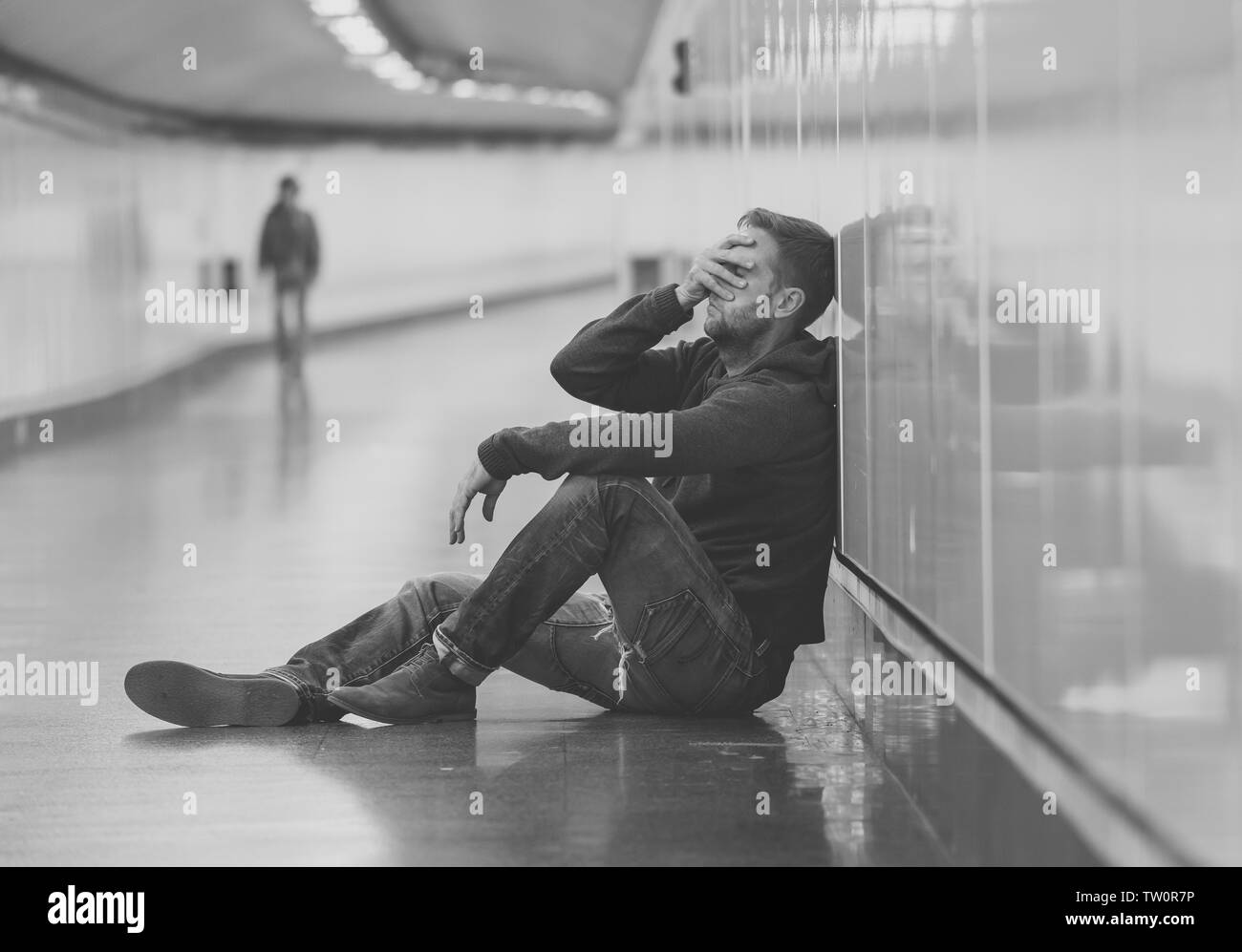 Sad young man crying suffering depression stress sitting on ground street subway tunnel looking desperate leaning on wall alone in Mental disorder Emo Stock Photo