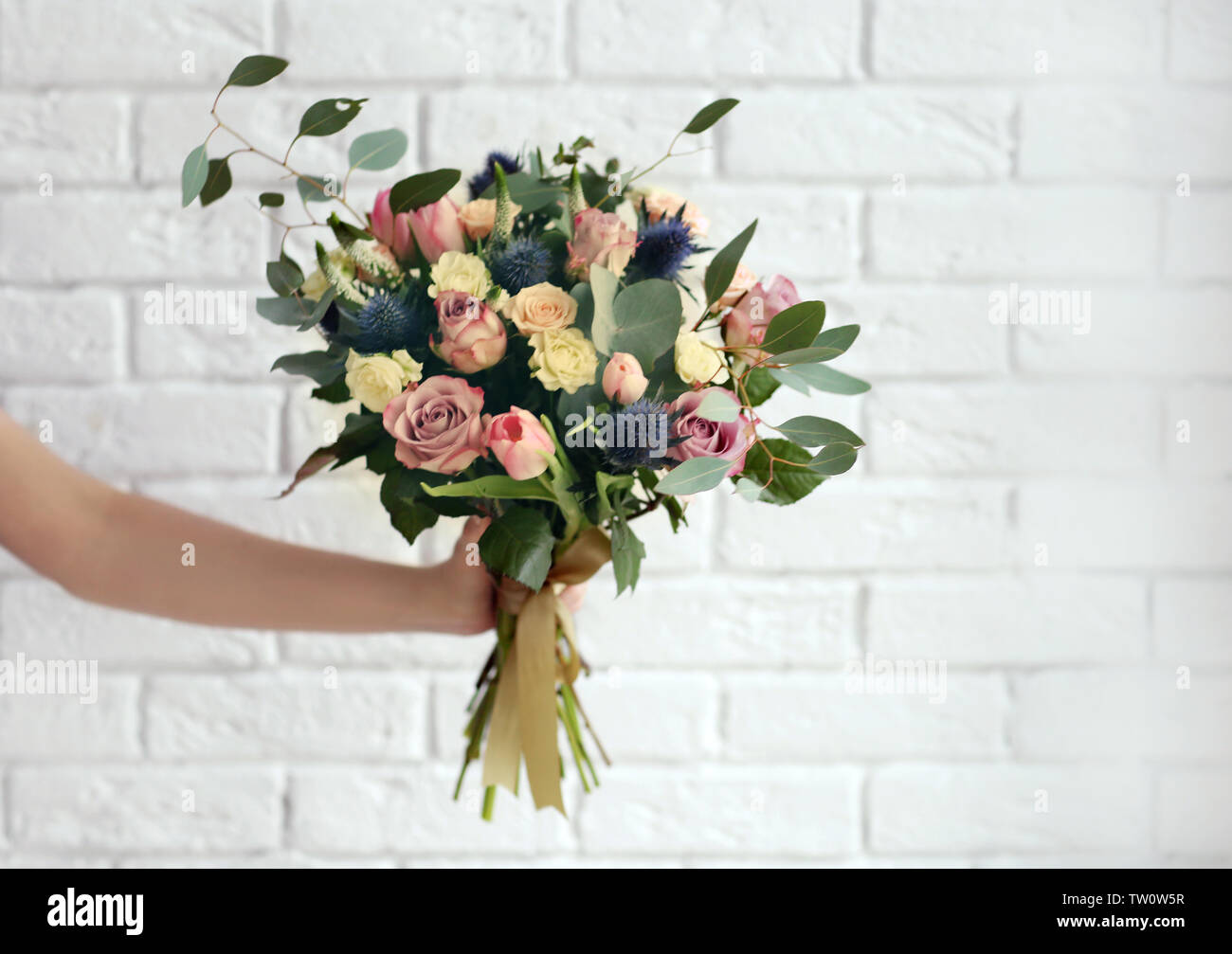 Female hand holding beautiful bouquet on brick wall background Stock
