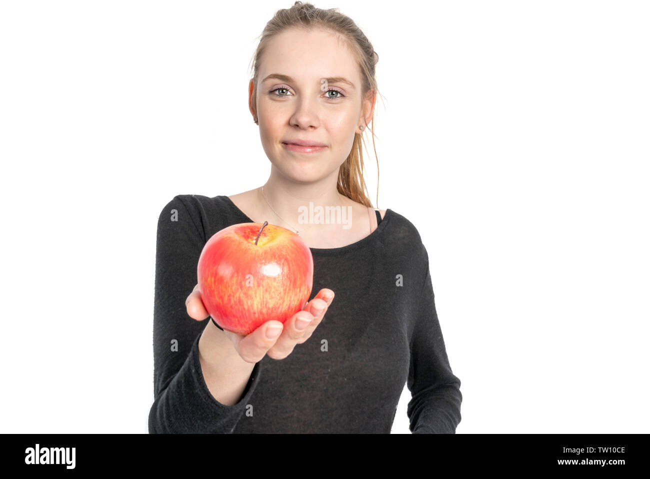 A young woman is holding an apple in her outstretched hand and smiling Stock Photo
