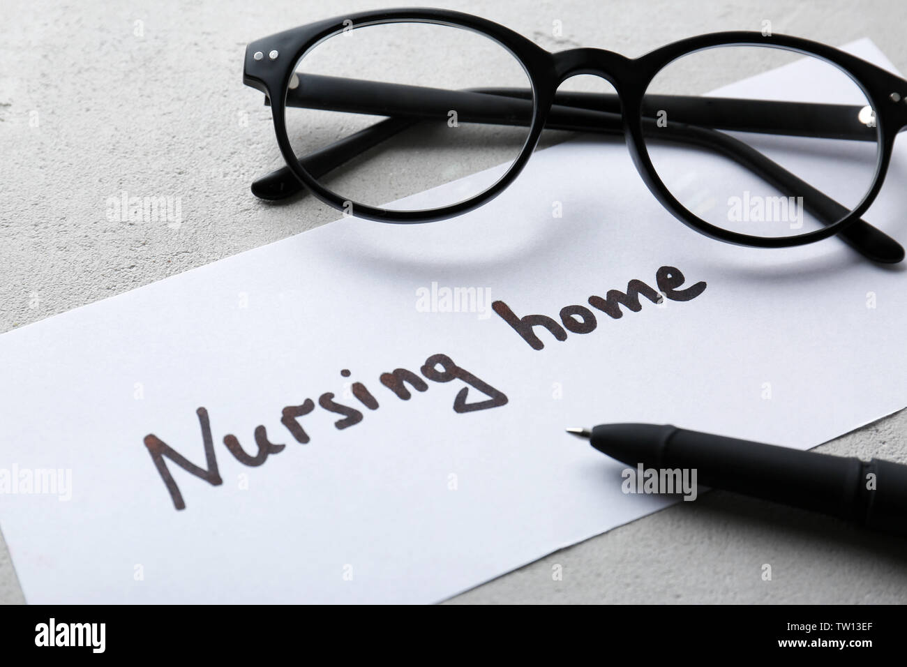 Eyeglasses and paper sheet with text NURSING HOME on light background