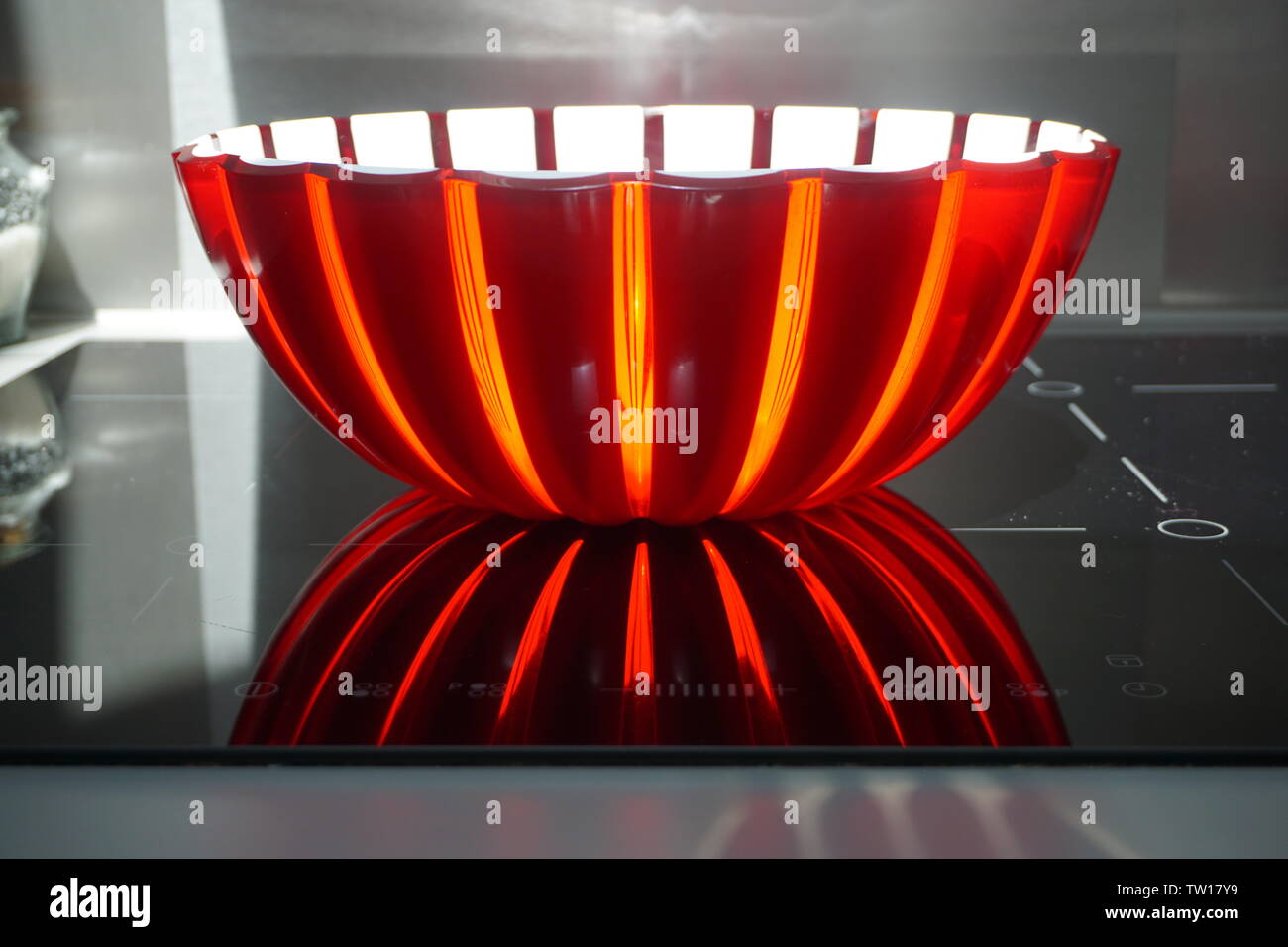 sun shining through a red and white plastic bowl on the stove Stock Photo