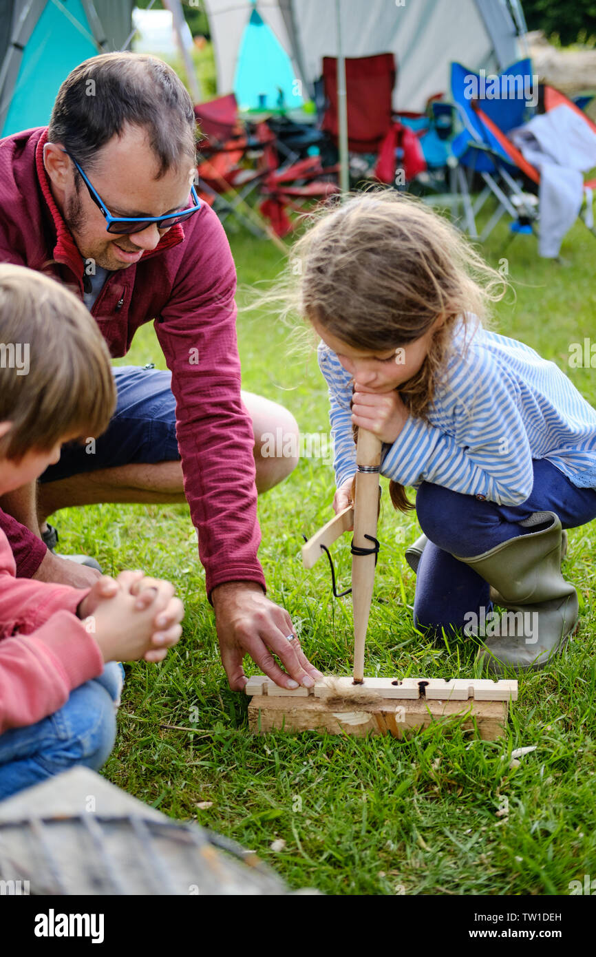 The Forest of Dean / UK - June 15th 2019: A father teaches a child to lite a fire using traditional friction techniques from a forest school on a camp Stock Photo