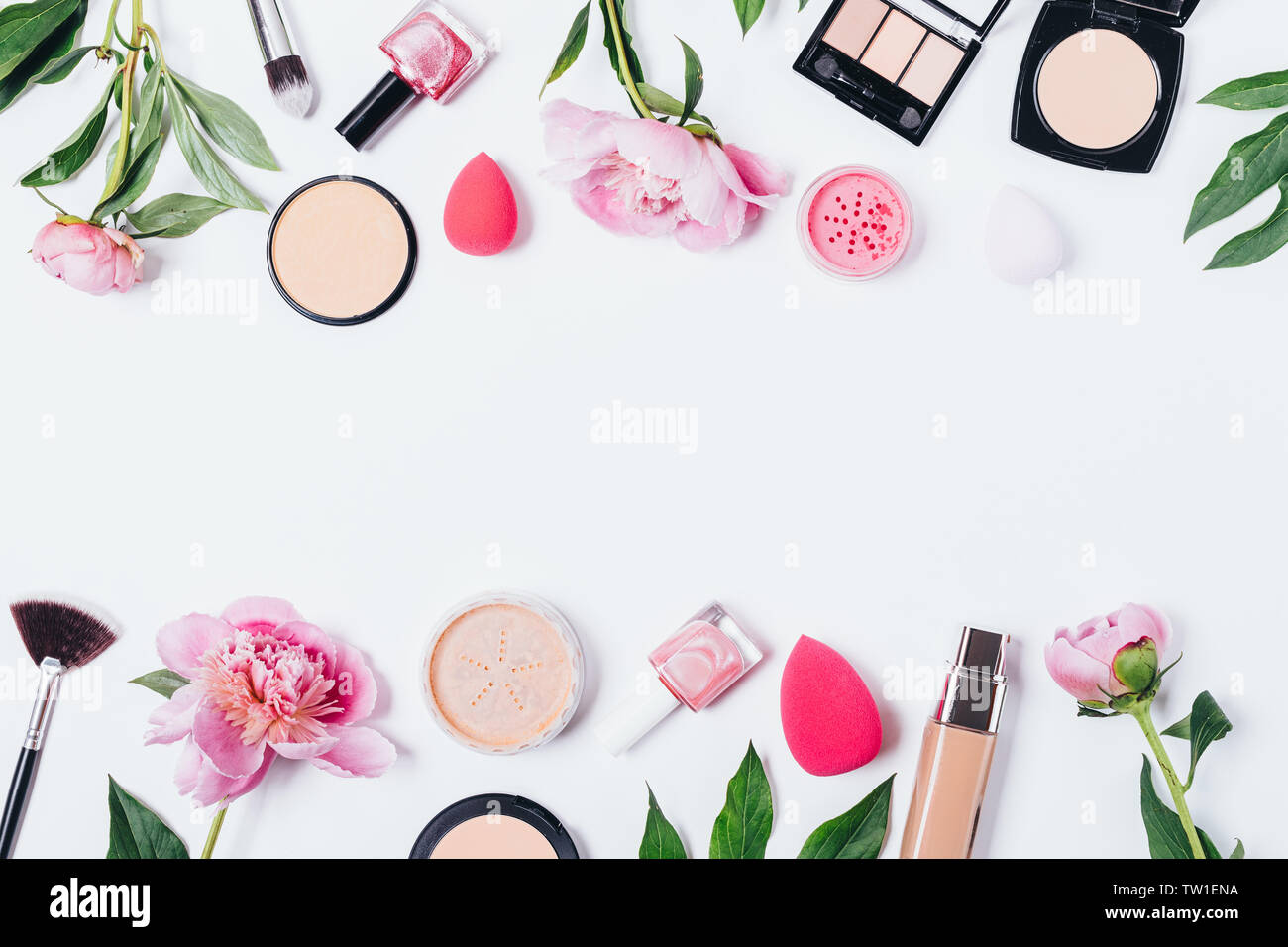 Floral makeup background of peonies next to cosmetic products and accessories on white table with an horizontal empty space in middle, flat lay. Stock Photo