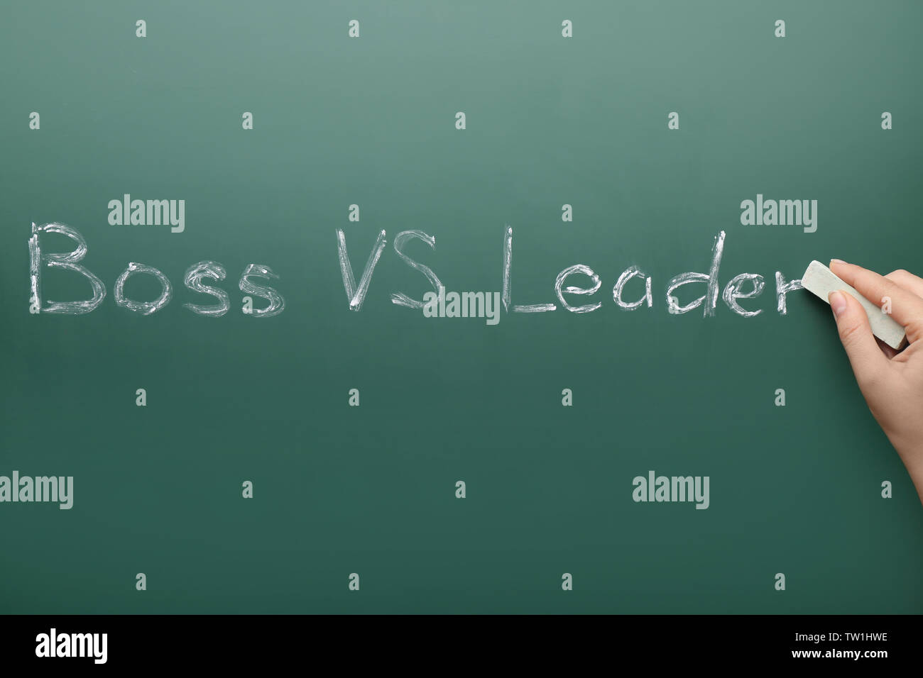 Female hand with chalk and words BOSS VS LEADER on chalkboard Stock