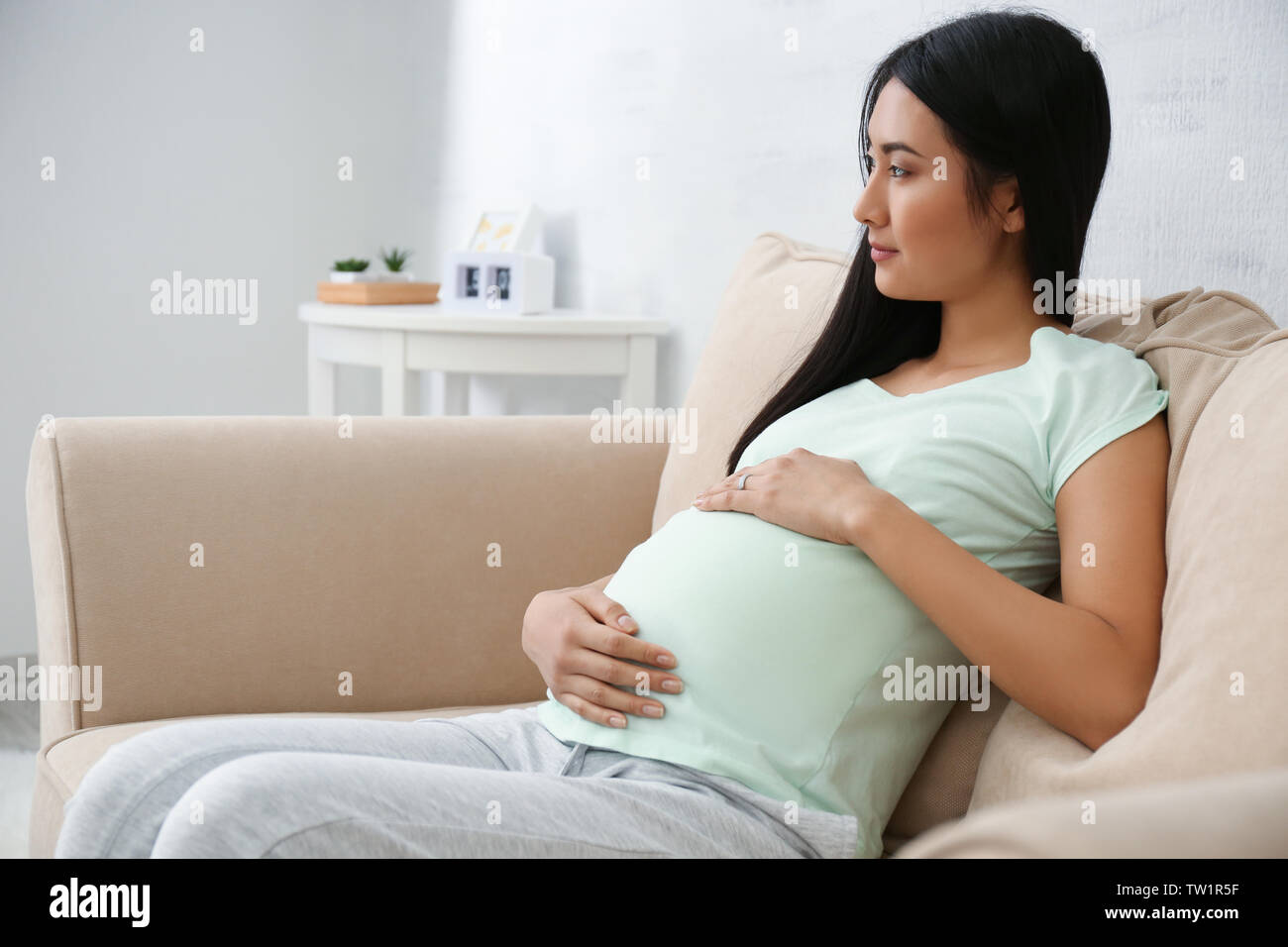 Pregnant Asian woman sitting on sofa at home Stock Photo Alamy