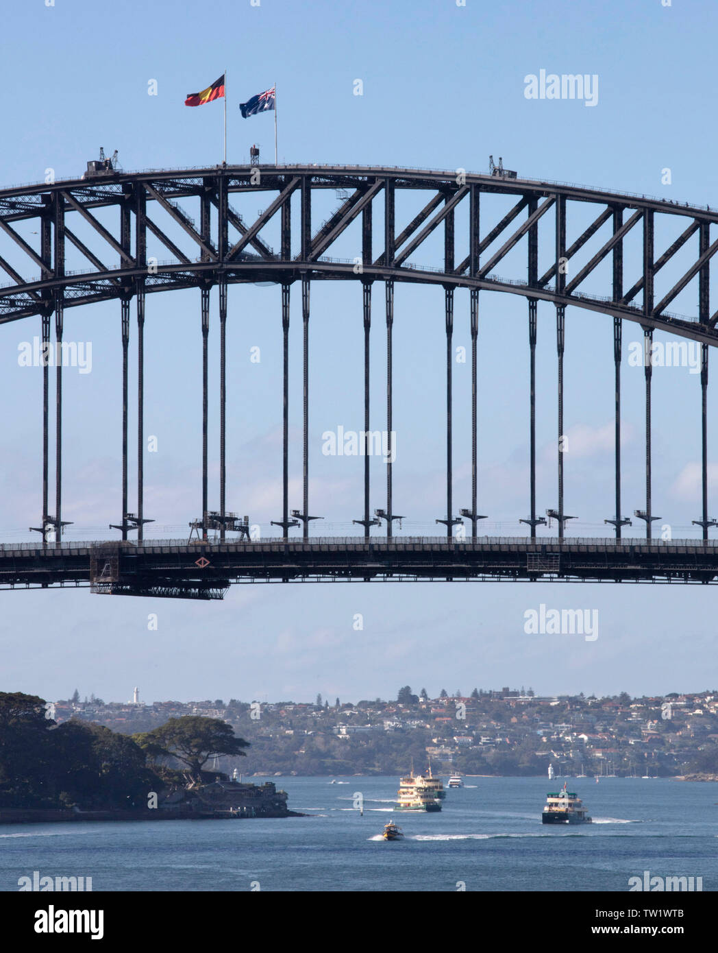 Detail of Sydney Harbor Bridge with national flag and aboriginal flag. Gardens of Admiralty house are situated at the bottom left. Boats are operating Stock Photo