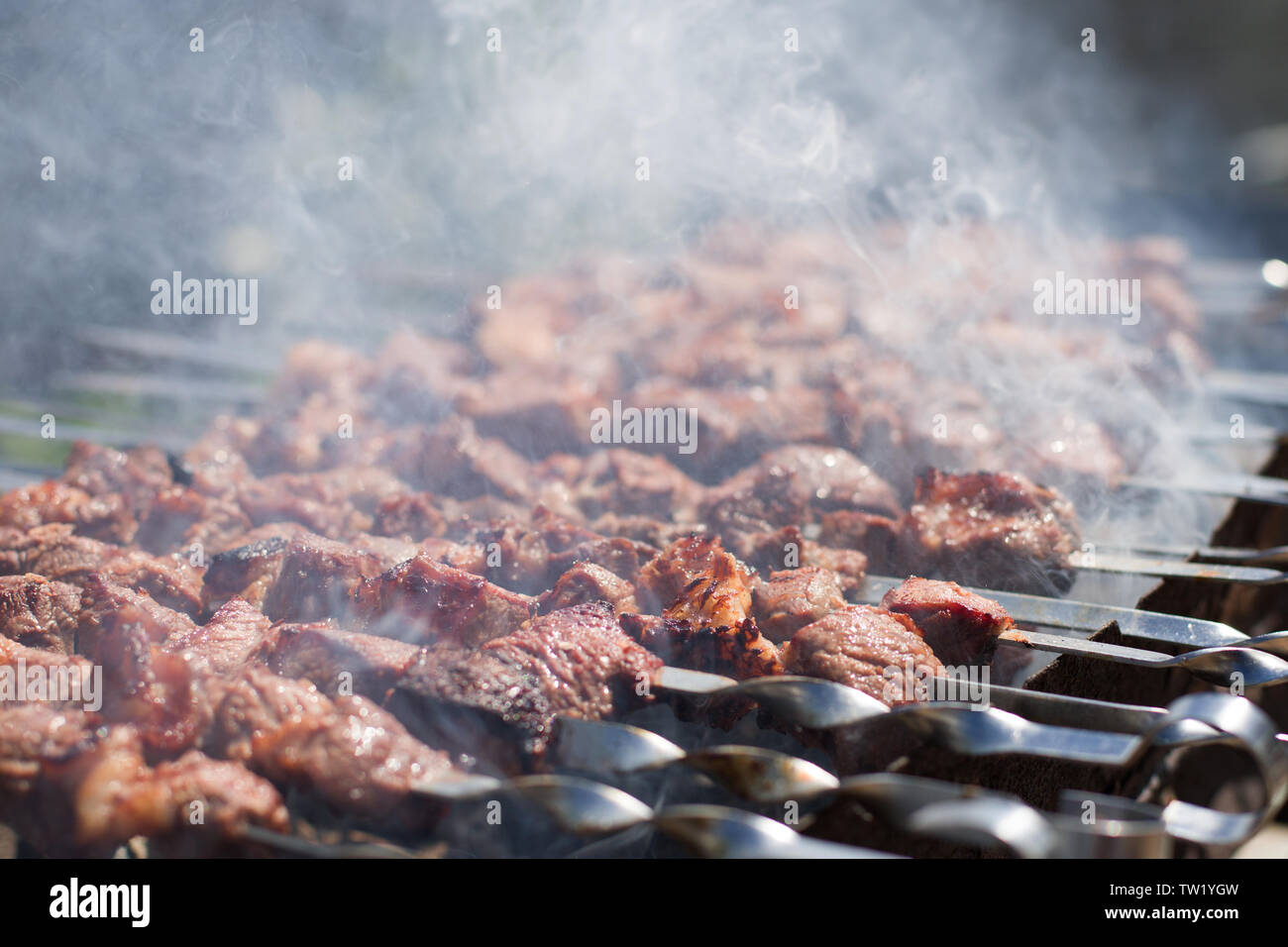 Shashlik or shashlyk preparing on a barbecue grill over charcoal. Grilled cubes of pork meat on metal skewer. Meat on skewers is roasted on fire. Stock Photo