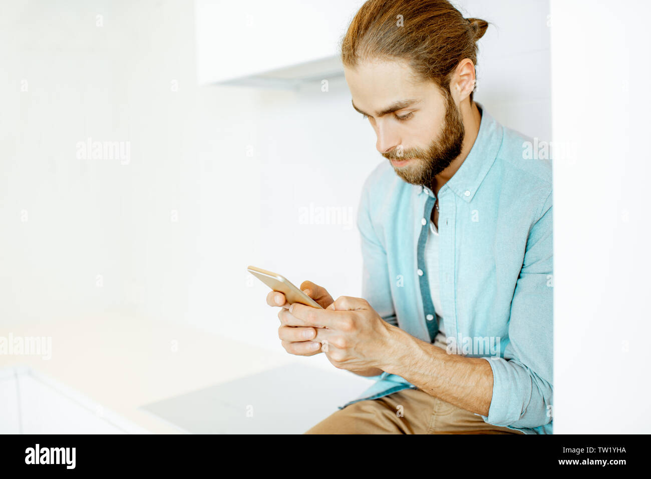 Handsome man using phone while sitting on the white kitchen at home Stock Photo