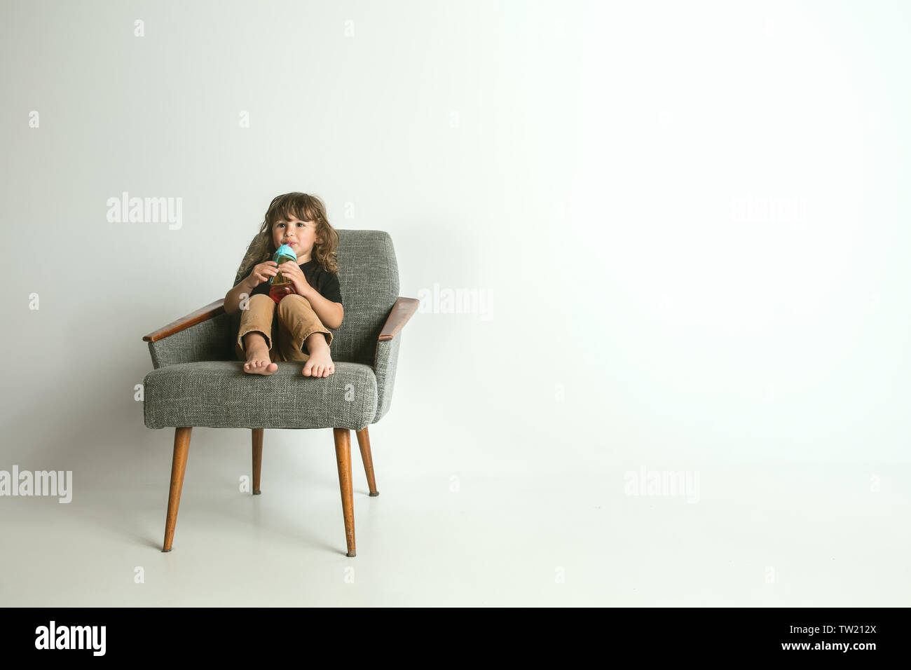 Little child sitting and playing in armchair isolated on white studio ...
