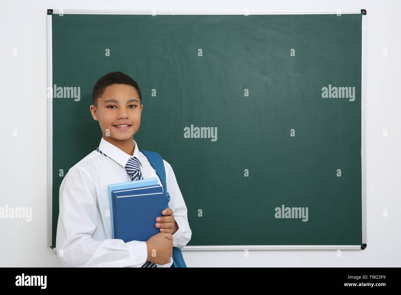 Cute boy with backpack and books standing near green school blackboard ...