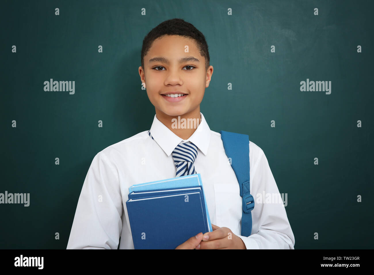 Cute boy with backpack and books standing near green school blackboard ...