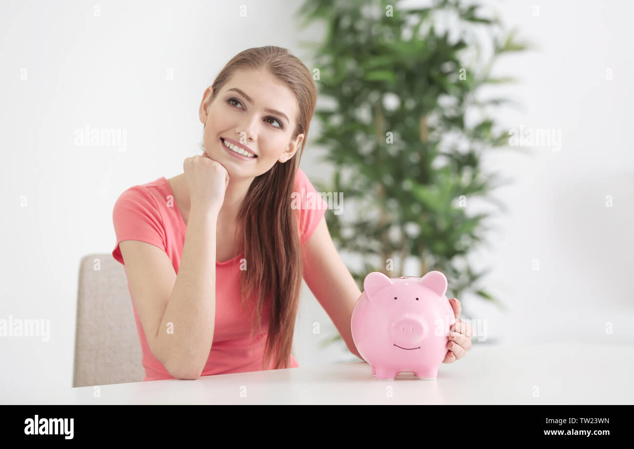 Beautiful young woman with piggy bank at home Stock Photo - Alamy