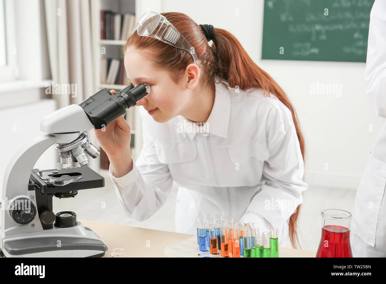 Beautiful school girl looking through microscope in chemistry class ...