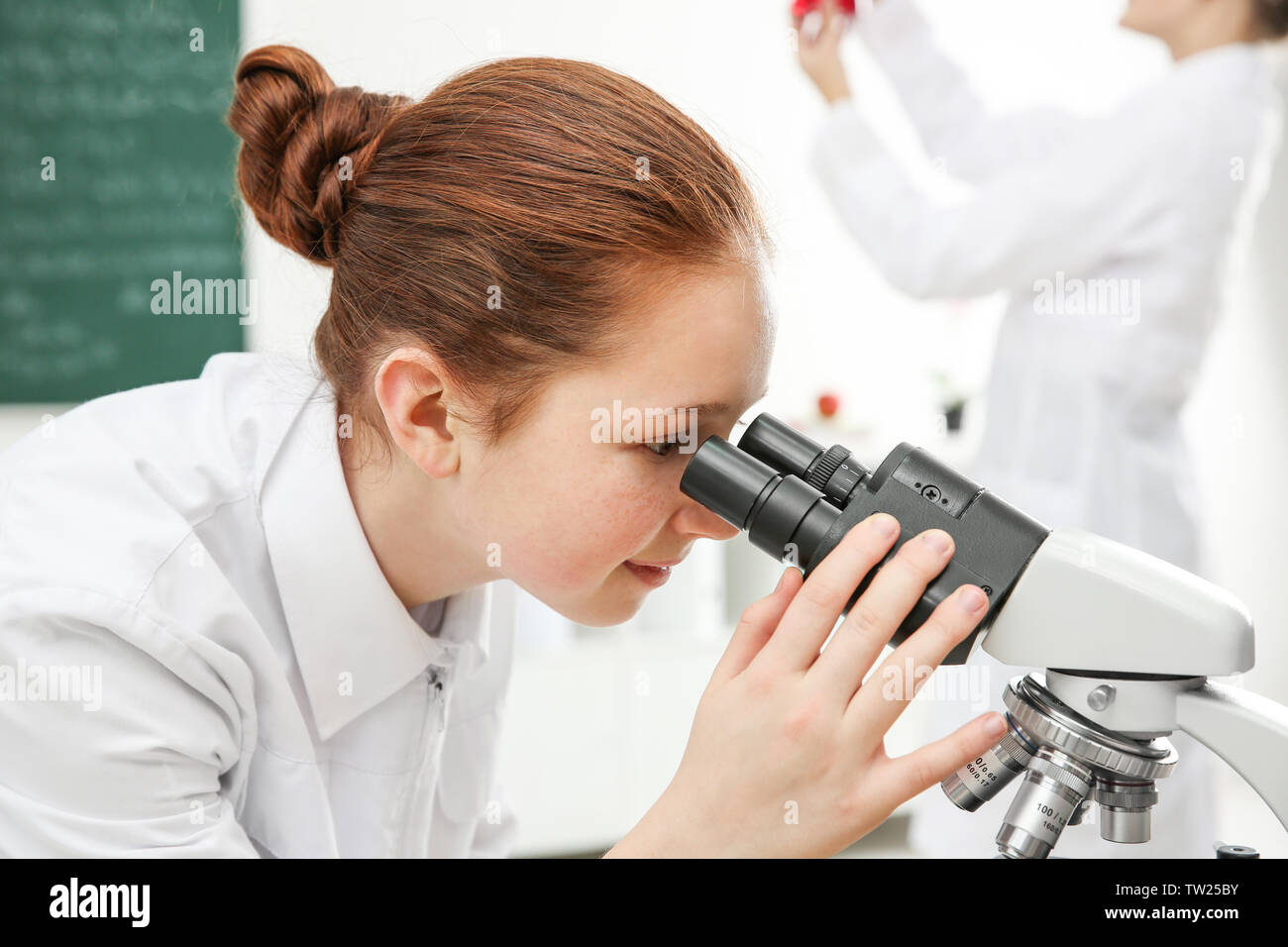 Beautiful school girl looking through microscope in chemistry class ...