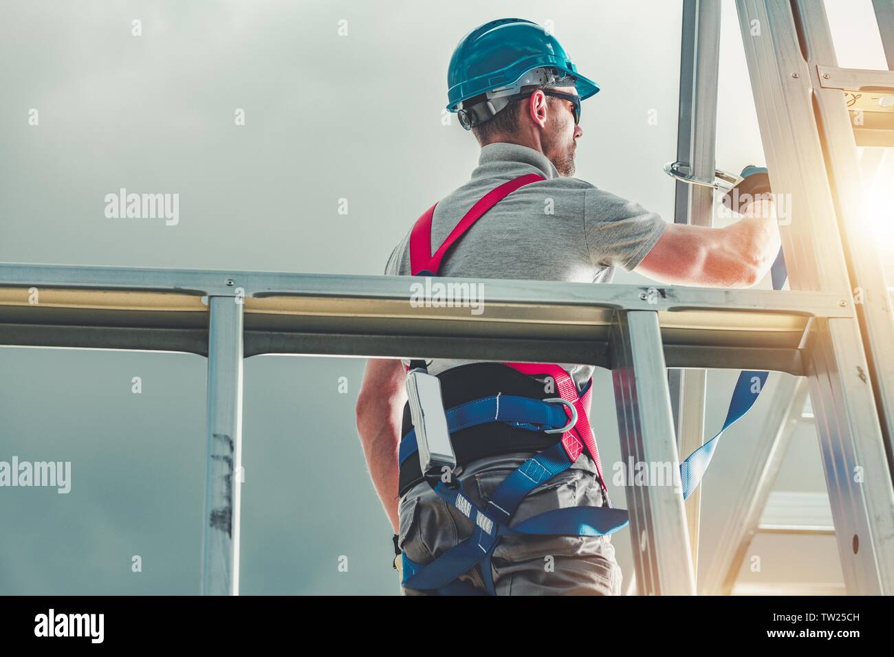 Caucasian Construction Contractor in His 30s Wearing Safety Harness. Steel House Building. Industrial Theme. Stock Photo