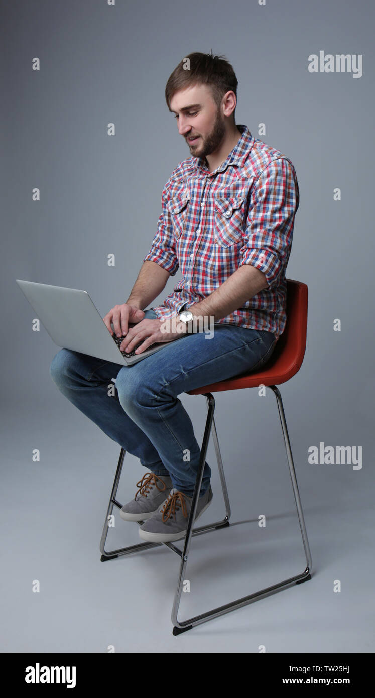 Young programmer sitting on chair and using laptop on light background ...