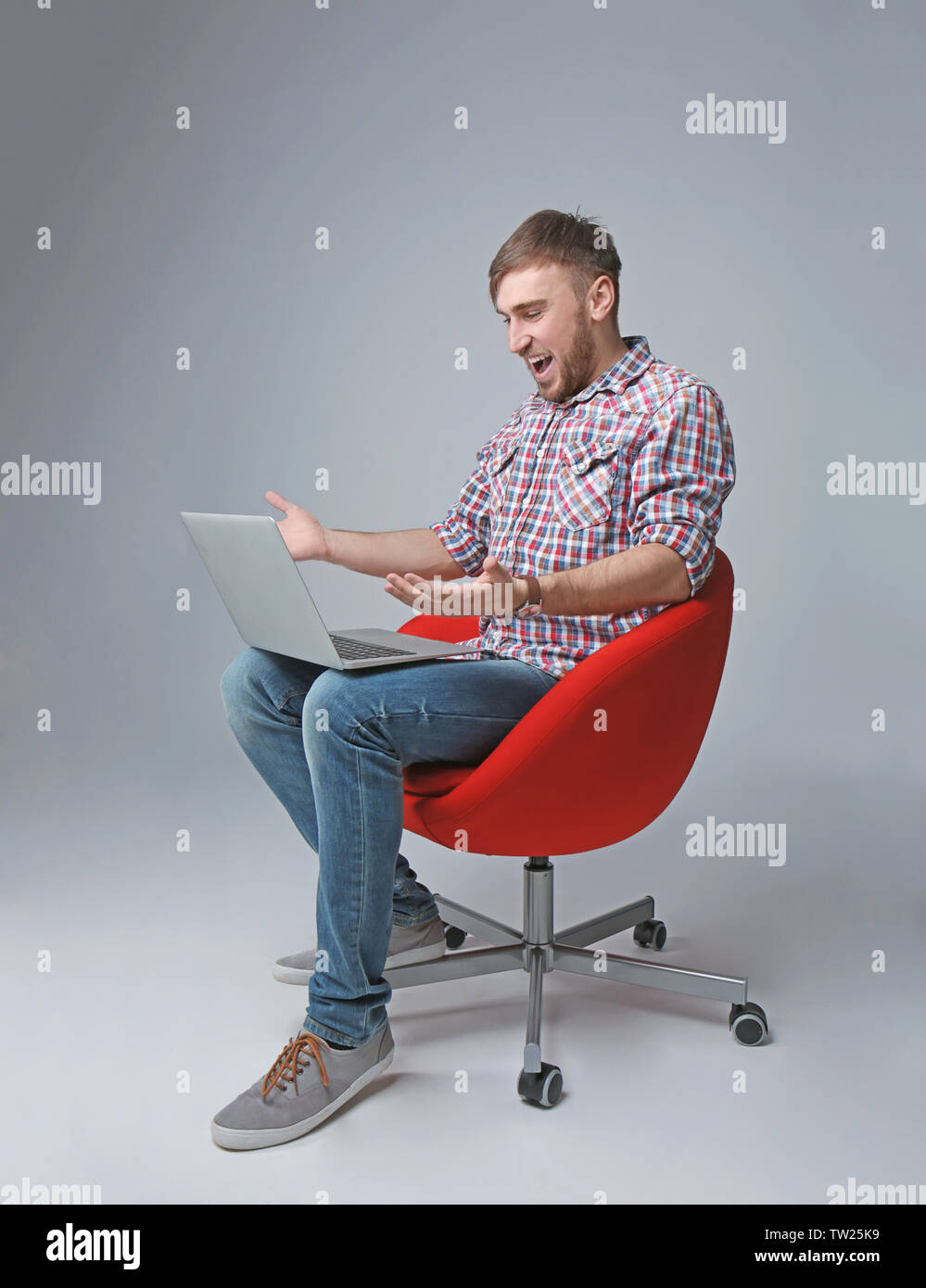 Young programmer sitting on chair and using laptop on light background ...