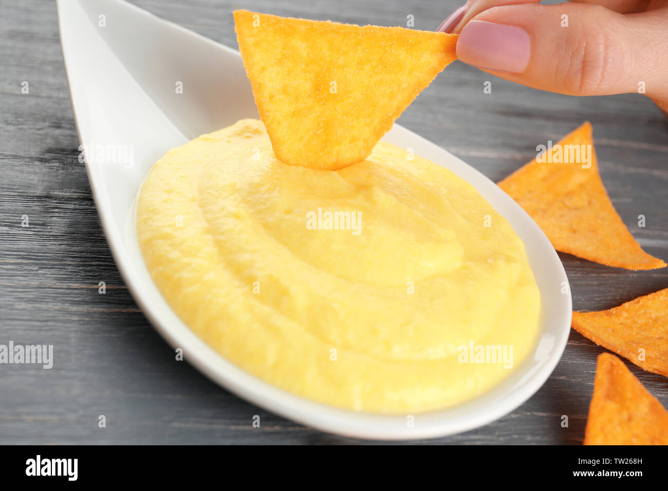 Dipping chips into bowl with cheese sauce on wooden table Stock Photo