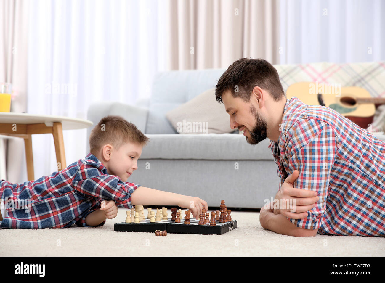 Father and son playing chess while lying on floor at home Stock Photo
