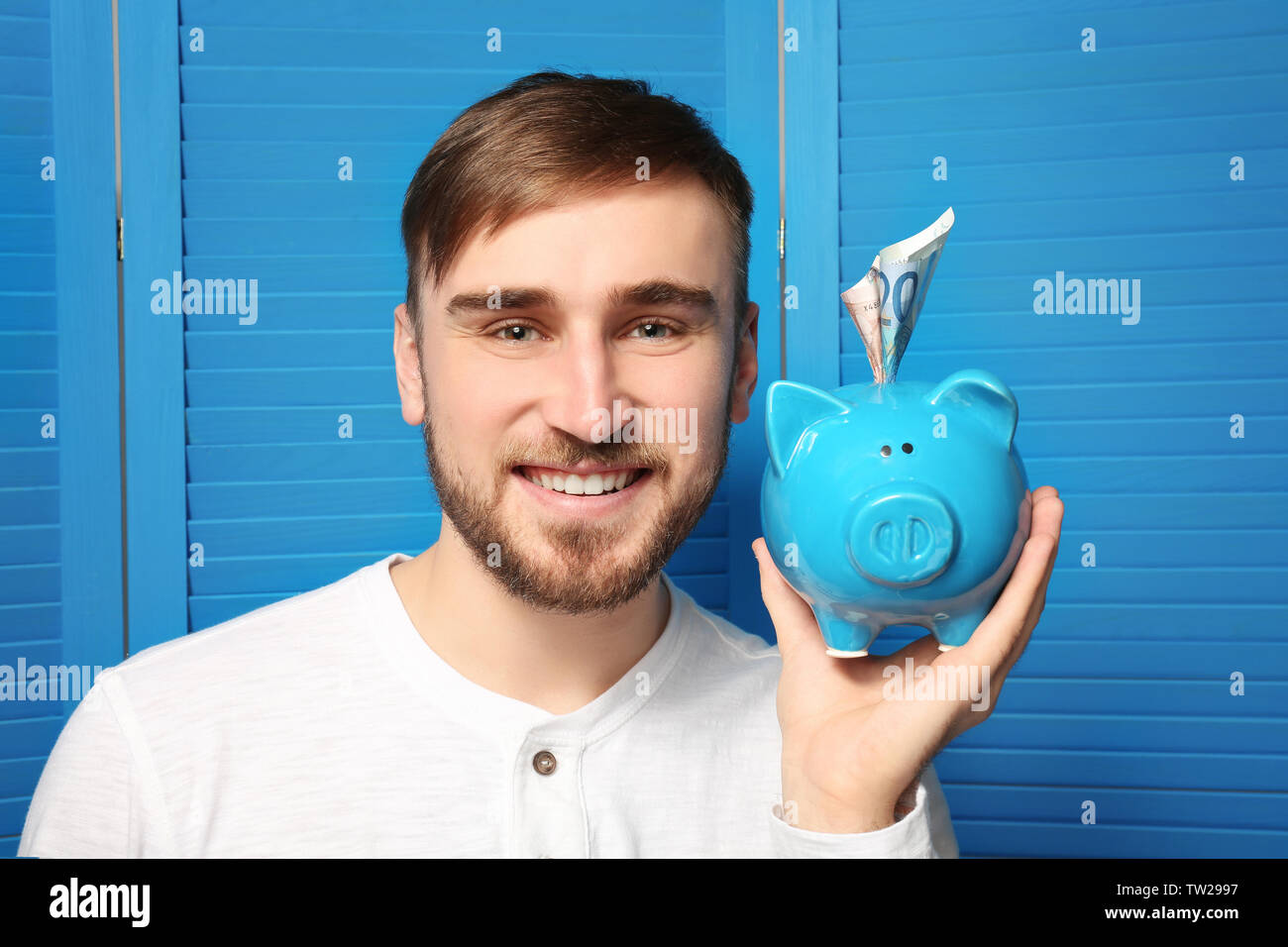 Happy young man holding piggy bank with money on color folding screen ...