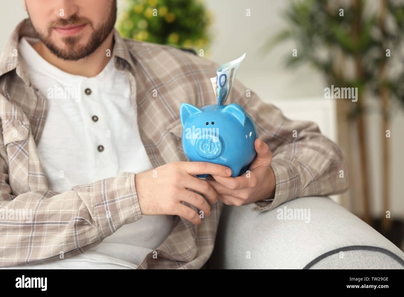 Happy young man sitting on sofa with piggy bank Stock Photo - Alamy