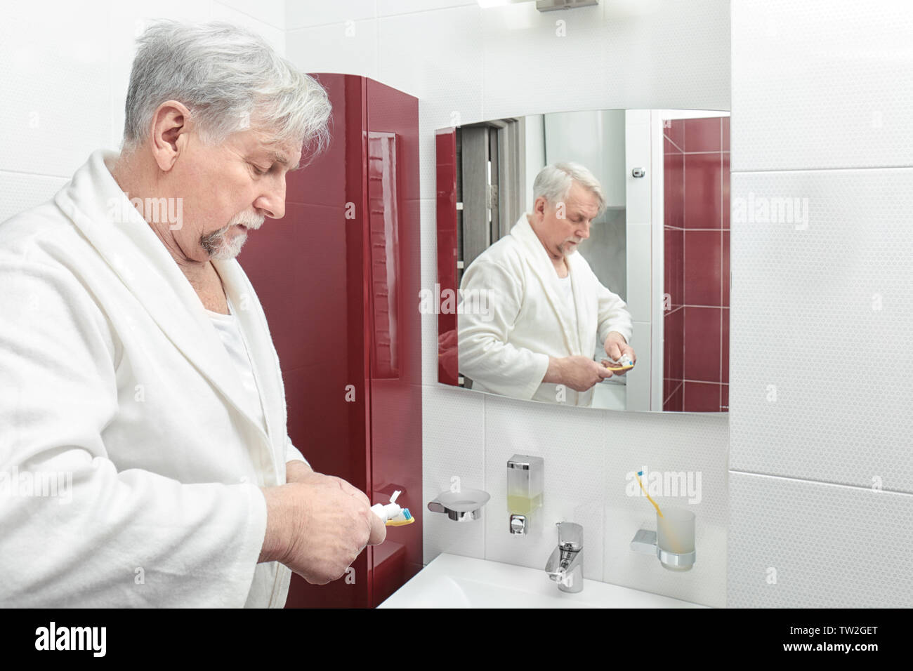 Elderly man brushing teeth in bathroom Stock Photo