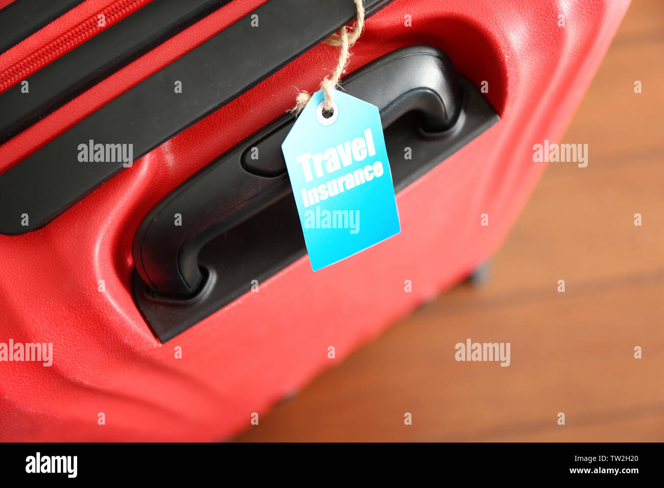 Red suitcase with label, closeup. TRAVEL INSURANCE concept Stock Photo