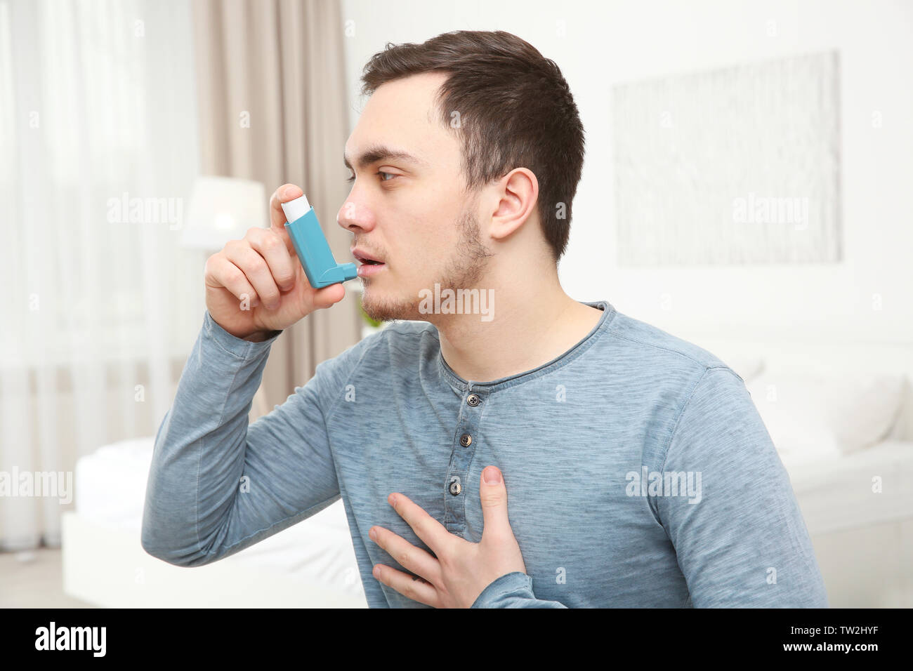 Young man using inhaler during asthmatic attack at home Stock Photo