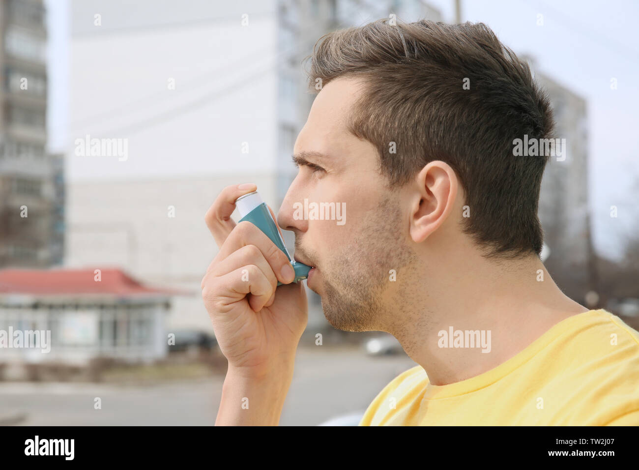 Young man using inhaler during asthmatic attack outdoors Stock Photo