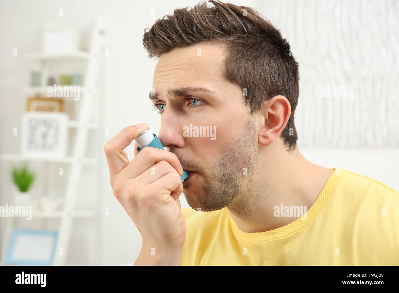Young man using inhaler during asthmatic attack at home Stock Photo