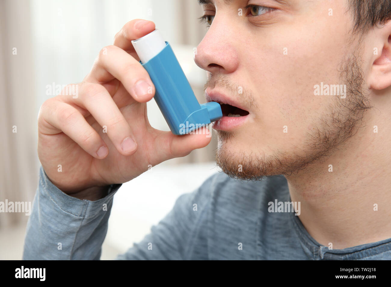Young man using inhaler during asthmatic attack at home, closeup Stock Photo