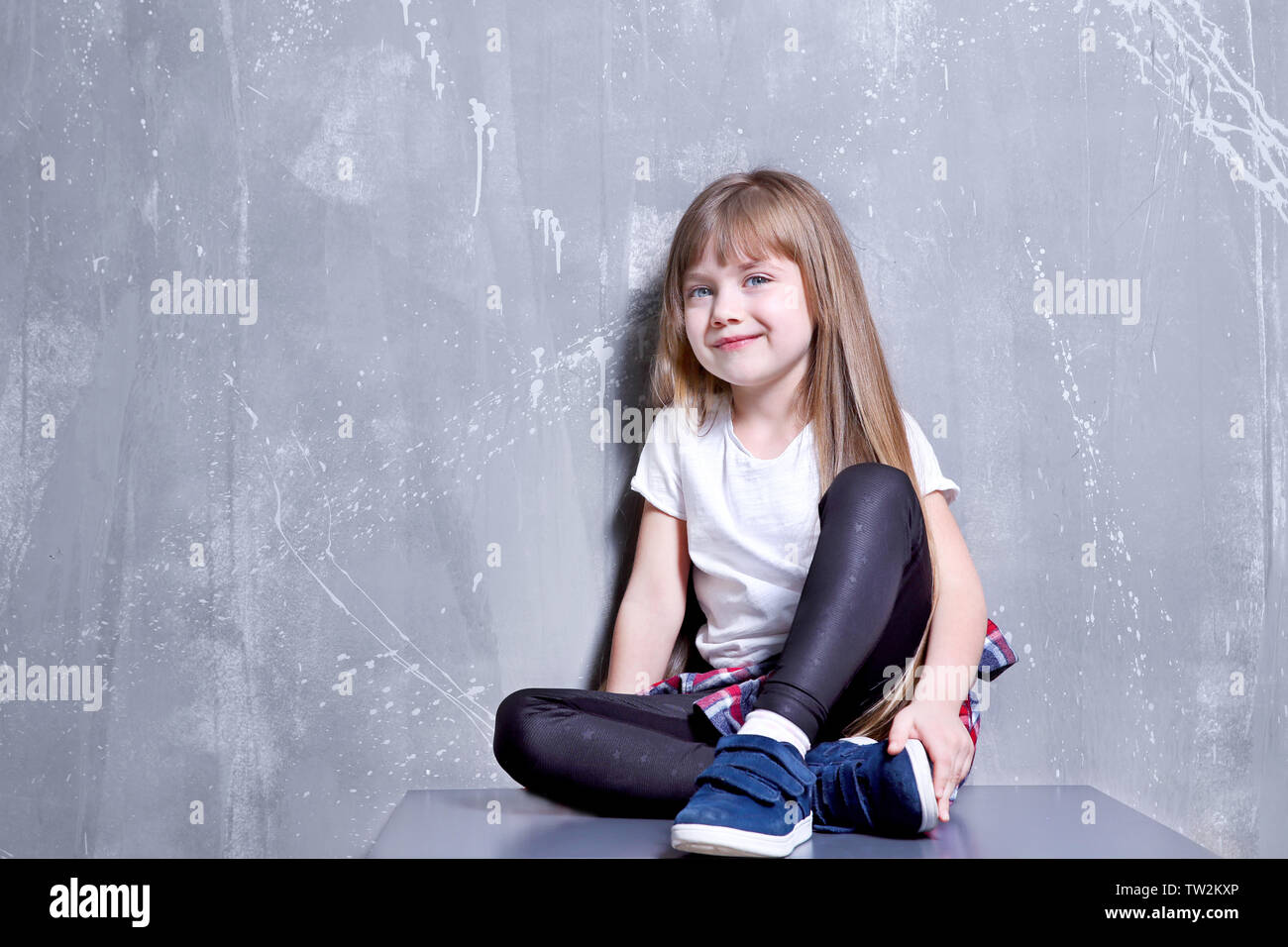 Cute Little Girl Sitting On Chest Of Drawers Against Textured Wall