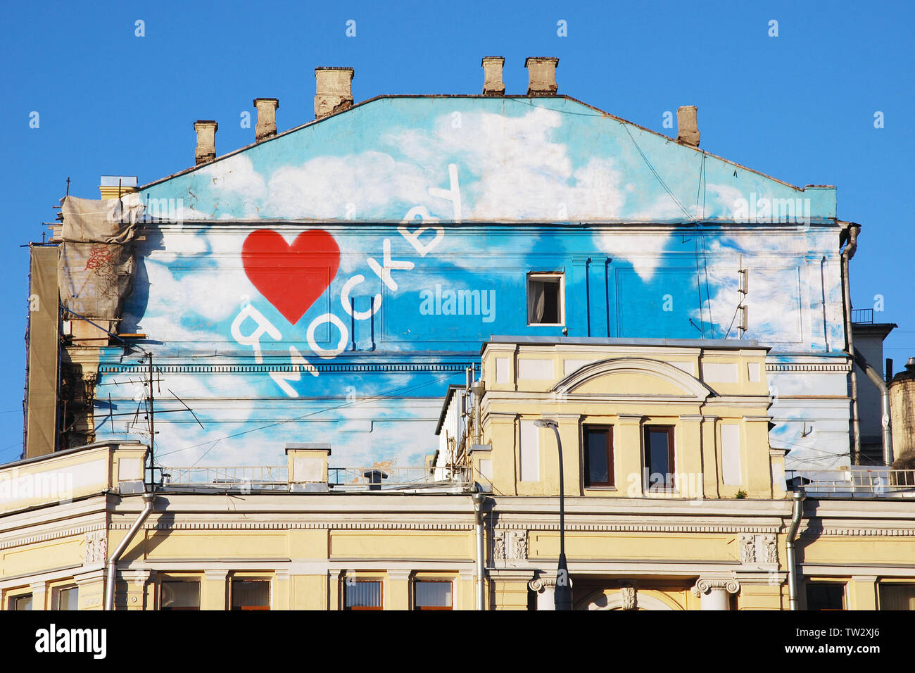 Inscription on old house roof in Russian 'I love Moscow', red heart, blue sky, white clouds, pale yellow walls,open windows, chimneys, downpipes Stock Photo