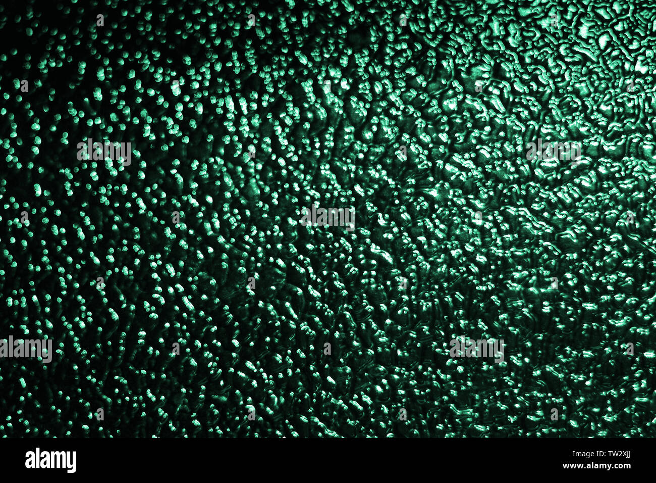 Abstract background of defocused mint green lights on dark background, glimpses of moon light on textured glass or water surface Stock Photo