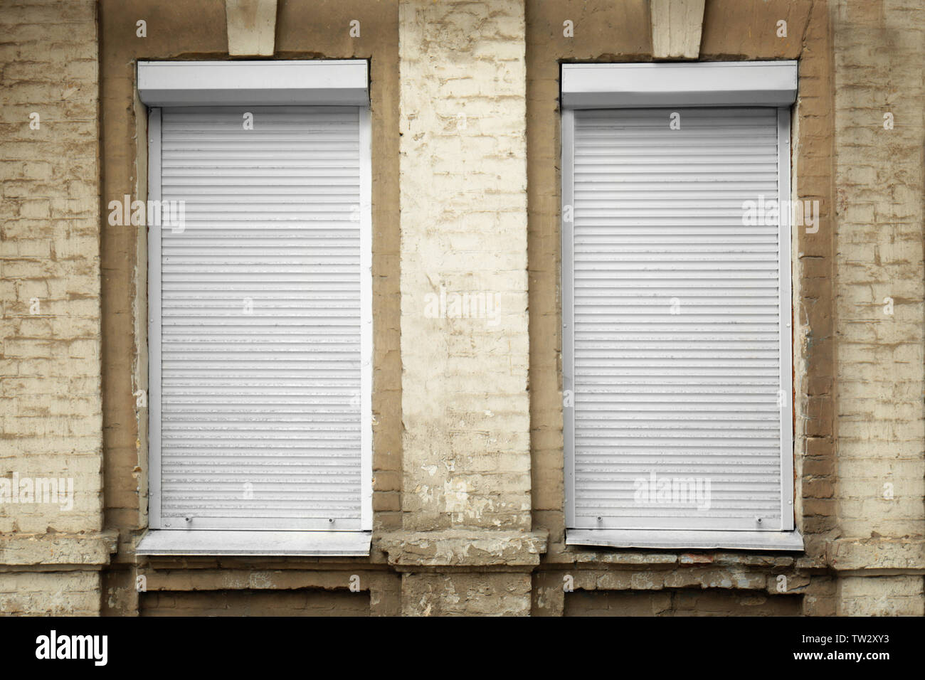 White windows with closed roller blinds in wall Stock Photo